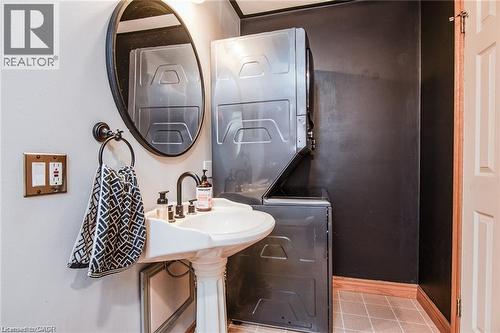 Pedestal sink with a matte black faucet, oval mirror, stacked washer and dryer, and tiled flooring - 67 Pinemeadow Crescent, Waterloo, ON - Indoor