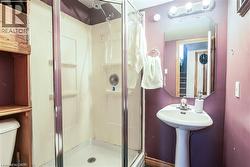 Three-piece bathroom featuring a pedestal sink with chrome faucet, octagonal mirror, and vanity lighting - 