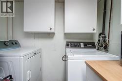 Dedicated laundry area featuring white wall cabinetry, a wood-finish countertop, and visible plumbing - 