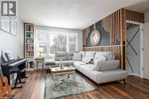 Living area with wood-finish flooring, a large window with white louvered blinds, built-in shelving, and a decorative slatted wood accent wall - 67 Pinemeadow Crescent, Waterloo, ON - Indoor Photo Showing Living Room