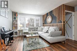 Living area with wood-finish flooring, a large window with white louvered blinds, built-in shelving, and a decorative slatted wood accent wall - 