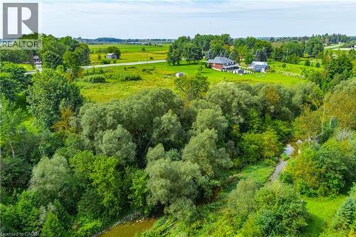 Lush green landscape featuring a natural waterway, mature trees, and open fields with distant structures - 7916 Wellington Road 109, Arthur, ON 