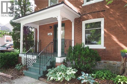 Brick facade featuring a white-trimmed covered porch with dark green steps - 148 Tiffany Street, Cambridge, ON - Outdoor With Exterior