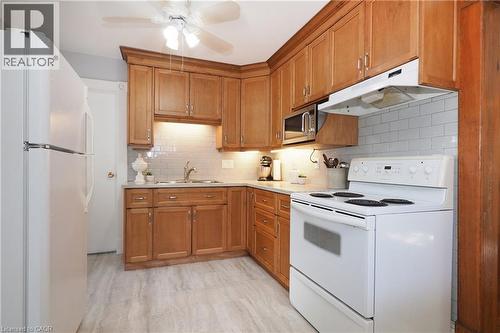Kitchen featuring wood cabinetry, white subway tile backsplash, light-toned flooring, white appliances, and a ceiling fan with integrated lighting - 148 Tiffany Street, Cambridge, ON - Indoor Photo Showing Kitchen With Double Sink