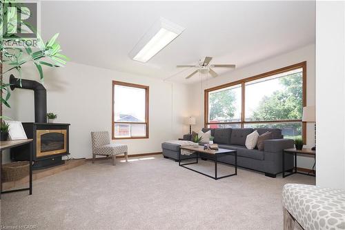 Spacious living area featuring light-colored carpeting, a black wood-burning stove with a gold-tone accent, and a wide window with wood trim - 148 Tiffany Street, Cambridge, ON - Indoor Photo Showing Other Room With Fireplace