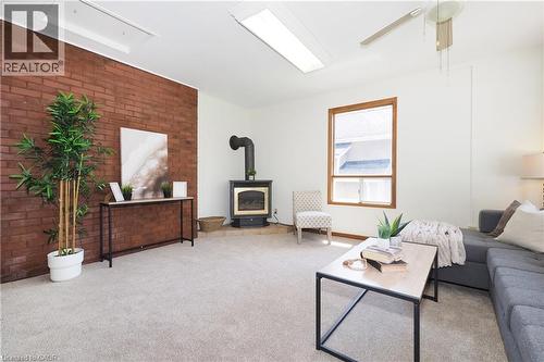 Living area with an exposed brick accent wall, light-toned carpeting, and a wood-burning stove with a black stovepipe - 148 Tiffany Street, Cambridge, ON - Indoor Photo Showing Living Room With Fireplace