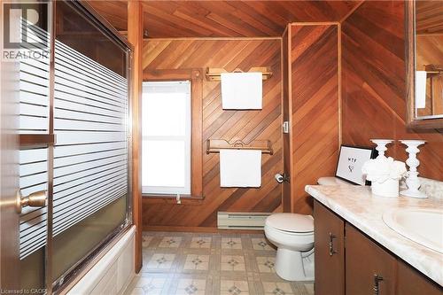 Bathroom featuring wood paneling, a shower-tub combination with a frosted glass enclosure, a single vanity with an integrated sink and light-colored countertop, a window with natural light, and patter - 148 Tiffany Street, Cambridge, ON - Indoor Photo Showing Bathroom