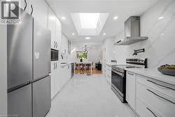 Gourmet kitchen featuring a large skylight, white cabinetry, integrated stainless steel appliances, white countertops, and a full-height backsplash - 