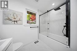 Modern bathroom featuring a bathtub with glass sliding doors, a black rain shower head, and white marble-look wall tiles - 