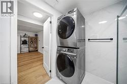 Stacked laundry machines within a utility space featuring white marble-look wall tiling and a glass shower enclosure - 