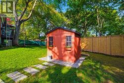 Vibrant red storage shed with black trim and window boxes, situated on a paver stone base - 