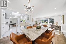 Open-concept dining area featuring a contemporary chandelier, wood-finish flooring, and a large window - 