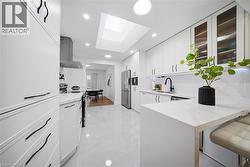 Contemporary kitchen featuring white cabinetry with black hardware, stainless steel appliances, a central skylight, and white tile flooring - 
