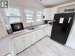 Kitchen featuring light-finish flooring, white cabinetry with silver hardware, light-toned countertops, and a double basin stainless steel sink with a gooseneck faucet - 