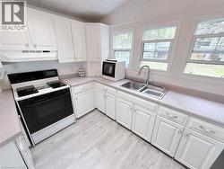 Kitchen featuring white cabinetry, light-toned countertops, a stainless steel double-basin sink, a black electric range, and light wood-finish flooring - 