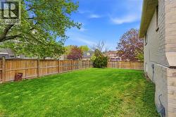 Expansive lawn area enclosed by a privacy fence, featuring a partial brick exterior and mature trees - 