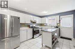 Bright kitchen featuring white cabinetry, stainless steel appliances, a tiled backsplash, and light-colored tiled flooring - 