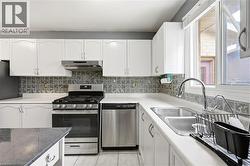 Kitchen featuring white cabinetry, a stainless steel gas range with overhead vent, a stainless steel dishwasher, a double basin stainless steel sink with a gooseneck faucet, and a patterned tile backs - 