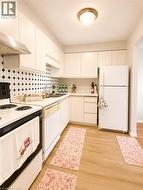 Kitchen featuring ample cabinetry, an integrated range hood, a tiled backsplash, wood-finish flooring, and a flush mount ceiling light fixture - 