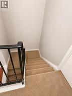 Staircase featuring neutral carpeting, a wrought iron railing, and white baseboards - 