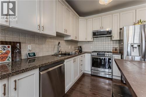 Kitchen featuring white cabinetry, dark granite countertops, stainless steel appliances, a tile backsplash, and dark wood-finish flooring - 2121 Prospect Street, Burlington, ON - Indoor Photo Showing Kitchen With Double Sink With Upgraded Kitchen
