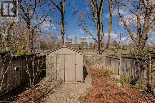 Rear yard featuring a storage shed on a paver patio with a curved pathway, surrounded by wood fencing and mature trees - 2121 Prospect Street, Burlington, ON - Outdoor