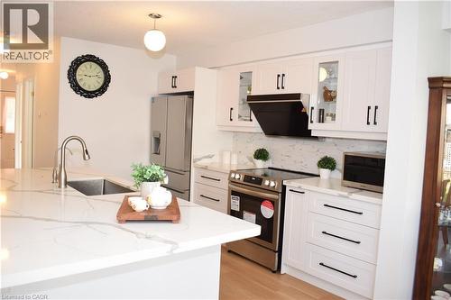 Kitchen featuring an expansive island with an undermount sink, white cabinetry with black hardware, stainless steel appliances, and wood-finish flooring - 28 Lemon Grass Street, Kitchener, ON - Indoor Photo Showing Kitchen With Upgraded Kitchen