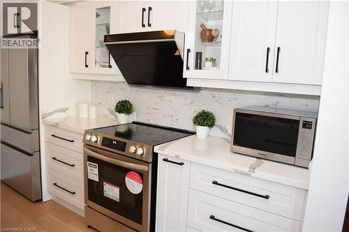 Contemporary kitchen featuring white cabinetry with black hardware, stone-finish countertops, stainless steel appliances, and a tiled backsplash - 28 Lemon Grass Street, Kitchener, ON - Indoor Photo Showing Kitchen