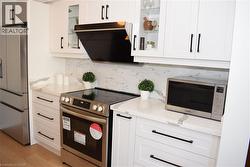 Contemporary kitchen featuring white cabinetry with black hardware, stone-finish countertops, stainless steel appliances, and a tiled backsplash - 