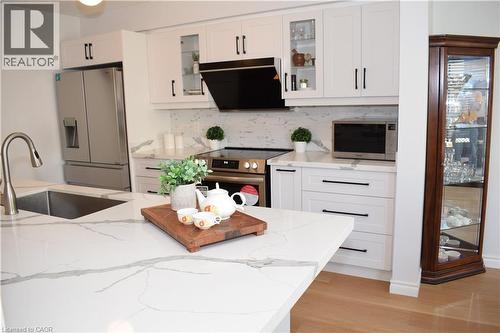 Modern kitchen featuring white shaker cabinetry with black hardware, a large island with a waterfall edge countertop, stainless steel appliances, and wood-finish flooring - 28 Lemon Grass Street, Kitchener, ON - Indoor Photo Showing Kitchen With Upgraded Kitchen