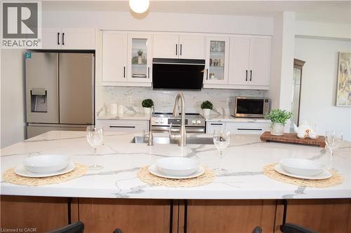 Kitchen featuring a large central island with a built-in sink and stainless steel faucet, white cabinetry with black hardware, stainless steel appliances, and a matching stone countertop and backsplas - 28 Lemon Grass Street, Kitchener, ON - Indoor Photo Showing Kitchen