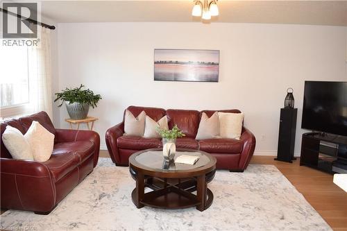 Open concept living area featuring light wood-finish flooring, a contemporary ceiling light fixture, and a large window with sheer white curtains - 28 Lemon Grass Street, Kitchener, ON - Indoor Photo Showing Living Room