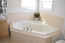 Corner jetted tub with chrome fixtures, surrounded by light-toned square tile - 
