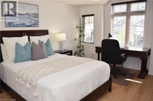 Bedroom featuring light wood-finish flooring, multiple windows with horizontal blinds, and a dark wood-finish desk area - 28 Lemon Grass Street, Kitchener, ON - Indoor Photo Showing Bedroom