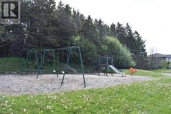 Outdoor recreational space featuring a swing set, playground structure with a slide, and a spring rider, all situated on a gravel surface - 