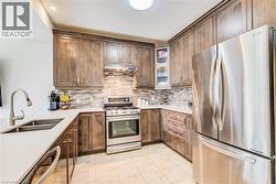 Kitchen featuring wood-finish cabinetry, stainless steel appliances, light-toned countertops, a mosaic tile backsplash, and tile flooring - 