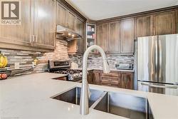 Modern kitchen featuring a double basin stainless steel sink, brushed nickel high-arc faucet, light-toned countertops, wood-finish cabinetry, and stainless steel appliances including a refrigerator, r - 