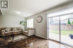 Spacious living area featuring wood-finish flooring, a neutral color palette, and a large window with blinds - 