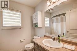 Bathroom featuring a vanity with an oval sink and a stone-finish countertop, an overhead wall-mounted cabinet, a window with horizontal blinds, a toilet, and a shower with a curtain - 