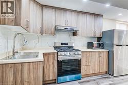 Kitchen featuring wood-finish cabinetry, stainless steel appliances, light-toned countertops, and a white tile backsplash with subtle veining - 