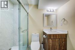 Modern bathroom featuring a glass-enclosed shower with tile surround, a wood-finish vanity with an integrated sink and light-colored countertop, and a wall-mounted mirror with overhead lighting - 
