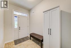 Entryway featuring light-toned tile flooring, a white paneled entry door with sidelight and transom window, and a built-in storage cabinet with black hardware - 