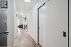 Entryway corridor featuring wood-finish flooring, white walls, recessed lighting, and a modern pocket door with a dark handle - 