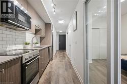 Galley kitchen featuring wood-finish cabinetry, stainless steel appliances, and a white subway tile backsplash - 