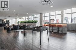Spacious common area featuring dark wood-finish flooring, a contemporary bar with tiled facade, expansive window walls, recessed lighting, and a foosball table - 