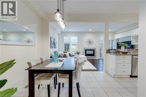 Combined kitchen, dining, and living areas featuring white tiled flooring, a linear pendant light fixture, a built-in fireplace, and a kitchen island with a mosaic tile backsplash - 598 Bessborough Drive, Milton, ON - Indoor Photo Showing Dining Room With Fireplace