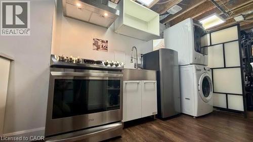 Stainless steel range with ventilation hood, stainless steel sink, under-sink cabinetry, stacked washer and dryer, and wood-finish flooring - 598 Bessborough Drive, Milton, ON - Indoor Photo Showing Laundry Room