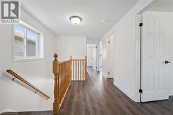 Upper-level hallway featuring wood-finish flooring, white walls, and multiple paneled doors with black hardware - 