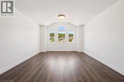 Spacious room featuring wood-finish flooring, white baseboards, and a vaulted ceiling - 