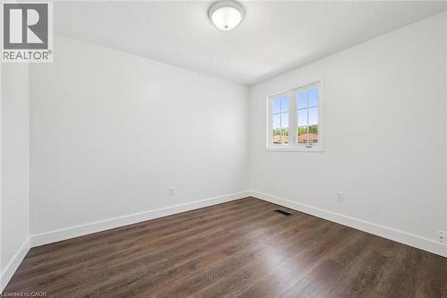 Room featuring wood-finish flooring, white baseboards, a single window with white trim, and a flush-mount ceiling light fixture - 71 Peach Blossom Crescent, Kitchener, ON 